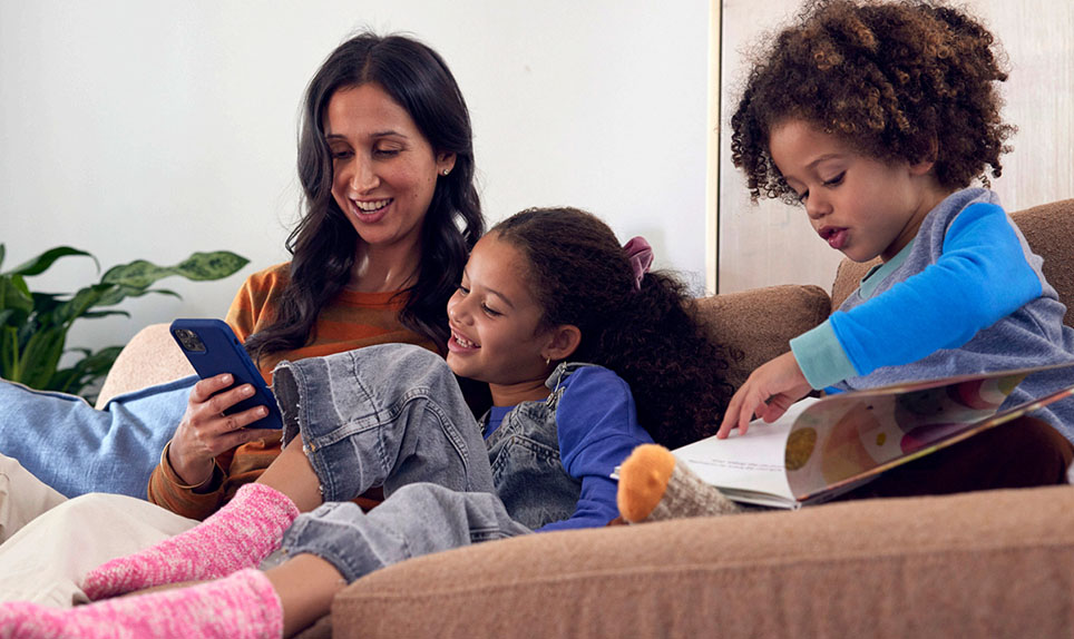 A family gathers on the couch and smiles while looking at a smartphone screen.