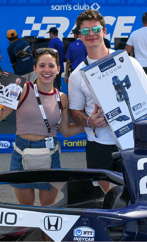 Two happy young people smile while holding products in front of a Sam's Club special event.